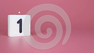 A square candle saying the number 1 being lit and blown out on a pink background celebrating a birthday