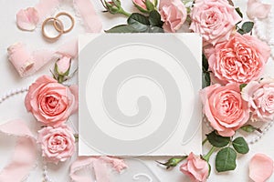 Square card near pink roses, wedding rings and silk ribbons top view, wedding mockup