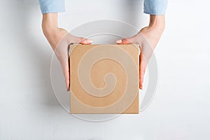 Square cardboard box in female hands. Top view, white background