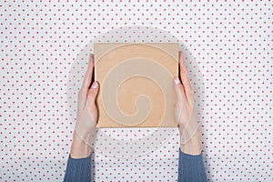 Square cardboard box in female hands. Top view, white background