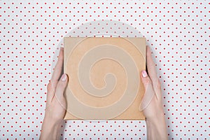 Square cardboard box in female hands. Top view, white background