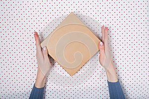 Square cardboard box in female hands. Top view, white background