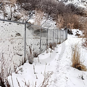 Square Chain link fence with barbed wires on snow covered hill slope viewed in winter