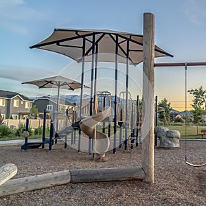 Square Childrens playground at a park with swings slides and umbrellas viewed at sunset