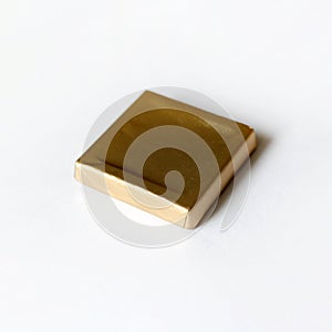 Square chocolate candy wrapped in golden foil isolated on white surface