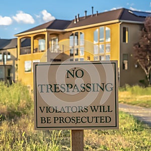 Square Close up of No Trespassing sign post beside a paved road that leads to houses