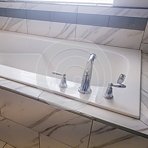 Square crop Close up of built in rectangular bathtub with stainless steel faucet and handles