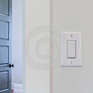 Square crop Electrical rocker light switch on white wall against blurry door background