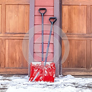 Square crop Red shovels on snowy driveway against wall and wooden garage doors of home