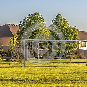 Square crop Soccer goal on vast green grassy field in front of houses viewed on a sunny day