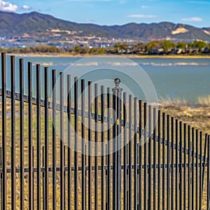 Square frame Black metal fence with a lake and grassy shore in the background