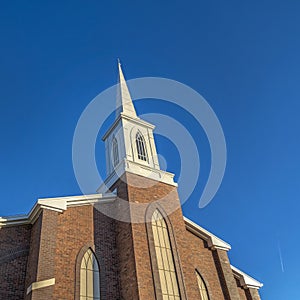 Square frame Church with classic red brick exterior wall and white steeple against blue sky