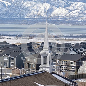 Square frame Church spire against neighborhood homes with snowy mountain and scenic lake view