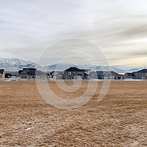 Square frame Grass covered terrain with distant snowy mountain and houses in the background