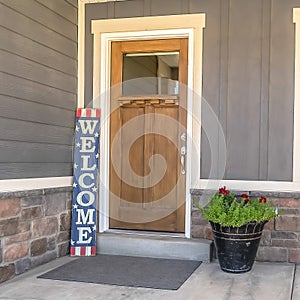 Square frame Home entrance with concrete porch brown wooden front door welcome sign