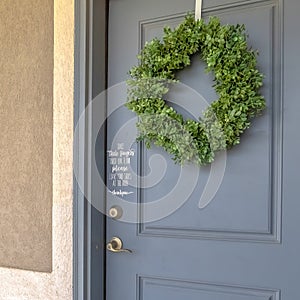 Square frame Home exetrior with close up on blue gray front door decorated with green wreath