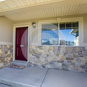 Square frame Home facade with maroon front door and combination of concrete and stone wall