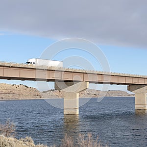 Square frame Huge trucks travelling on a massive bridge against snowy hills and cloudy sky