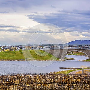 Square frame Lake with bank of stone and arched bridge under sky filled with clouds