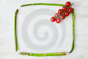 Square frame made with asparagus stems and decorated with a branch of cherry tomatoes in the corner