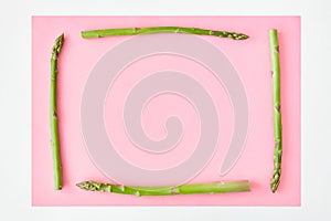 Square frame made with asparagus stems on the pink paper background with white borders.