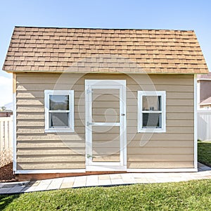 Square frame Shed at a backyard with roof shingles and vinyl wall siding