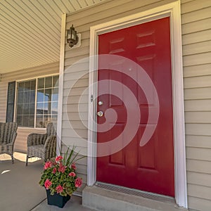 Square frame Shiny red wooden front door of a home with wicker chairs on the sunlit porch