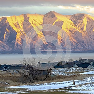 Square frame Snowy mountain lit by golden sun at sunset with lake and homes in the foreground