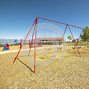 Square frame Swings on a park with playground pavilion lake and mountain in the background