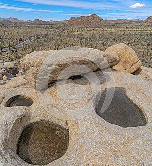 Square frame Three puddles on the rock with a view of a rocky mountains at Joshua Tree National Park, California