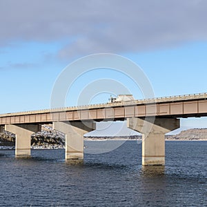 Square frame Truck travelling on a beam bridge over lake against rugged land and cloudy sky