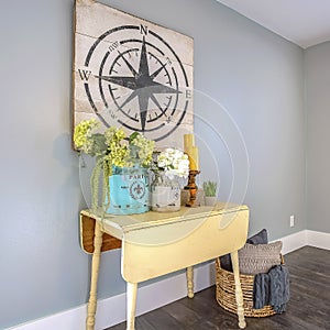 Square frame White table with ornaments and basket with pillows inside a room with wood floor