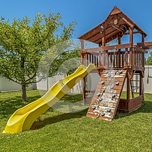 Square frame Wooden playground structure with yellow plastic slide swings and climbing wall