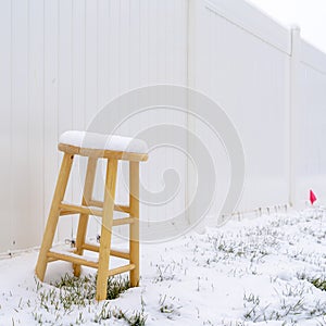 Square frame Wooden stool on snow covered ground in winter against white wood fence