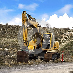 Square frame Yellow excavator and orange traffic delineator post beside a mountain road