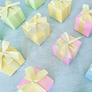 Square gift boxes in rainbow light gradient colors are neatly arranged on a blue-green watercolor textured background