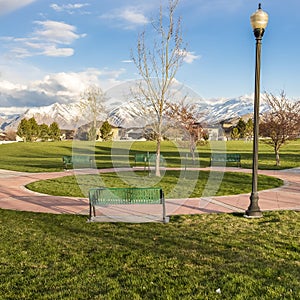 Square Green benches around a circular pathway on a park with trees and lamp posts