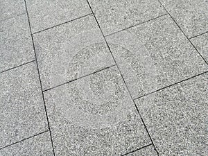Square grey tiles of a sidewalk in the city.