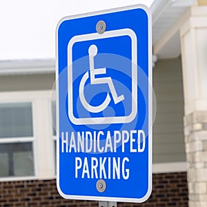 Square Handicapped Parking and Van Accessible sign against snow and building in winter