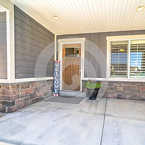 Square Home entrance with concrete porch brown wooden front door welcome sign