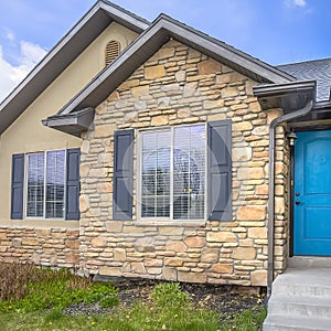 Square Home with stairs blue front door stone wall and windows with wooden shutters