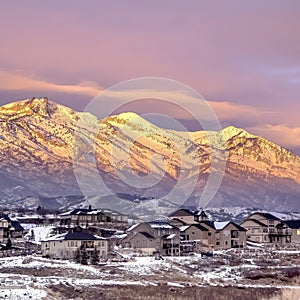 Square Homes on snowy hill against frosted Wasatch Mountain with golden glow at sunset