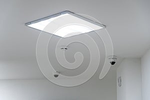 Square lamp and smoke detector on a white office ceiling. Round video surveillance lamps in the bank. Interior design in the