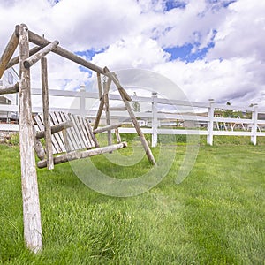 Square Old wooden garden swing on lush green grasses inside white picket fence