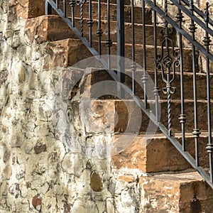 Square Outdoor staircase with stone steps and black metal railing against a fence