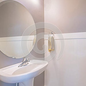 Square Pedestal sink with hanging towel on side and an oval mirror in a small bathroom