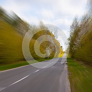 A square photo of fast traffic on an asphalt road through the forest