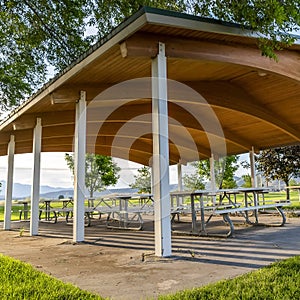 Square Picnic tables and benches under a pavilion on a scenic park on a sunny day