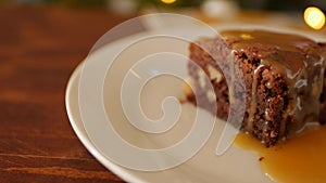 A square piece of chocolate brownie on a plate, on a wooden background, a napkin in yellow flowers and an old melchior