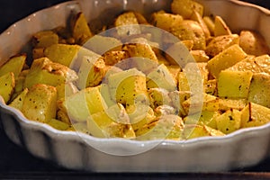 Square pieces of potatoes in olive oil are baked in the oven. Big dish wi